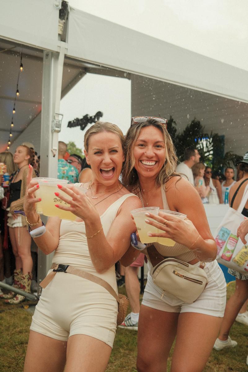 Two girls holding drinks in the rain at the 2024 Palm Tree Festival in the Hamptons